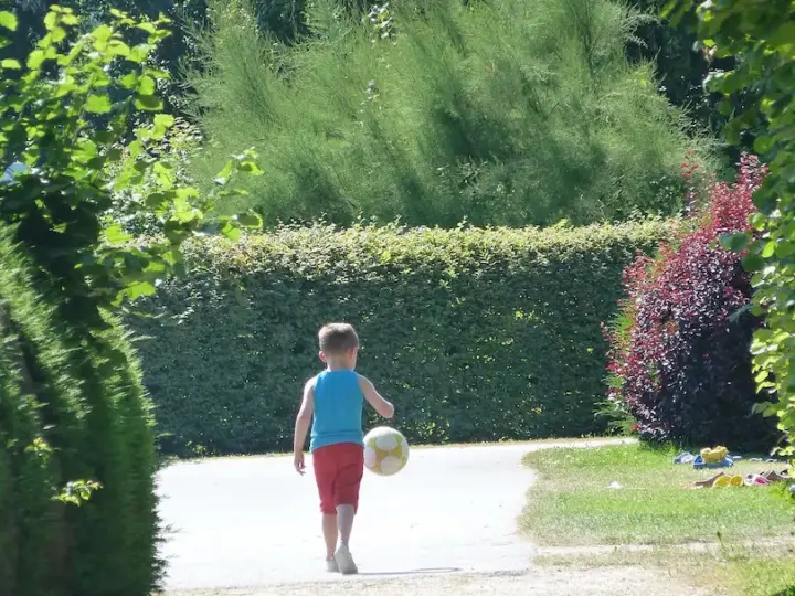 Petit garçon jouant au ballon dans un jardin verdoyant